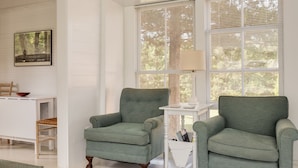A room with two green armchairs, a white table, and a framed picture on the wall.