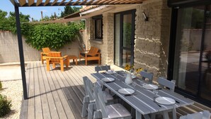 Eine Holzterrasse mit einer Pergola, einem Esstisch und zwei Holzsesseln.