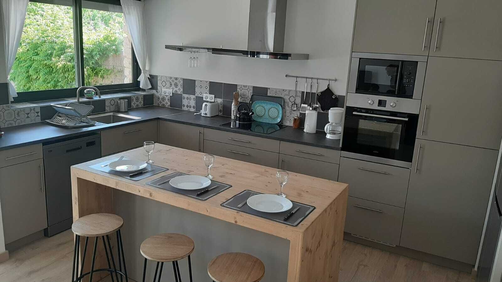 A modern kitchen with a central island, bar stools, a built-in oven, and a window with a view of greenery.