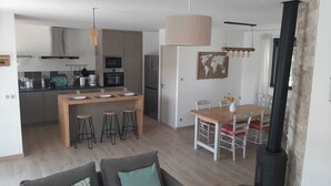 Eine moderne Küche mit einer zentralen Kochinsel, Barhocker, einem Esstisch mit Stühlen und einem Kaminofen.