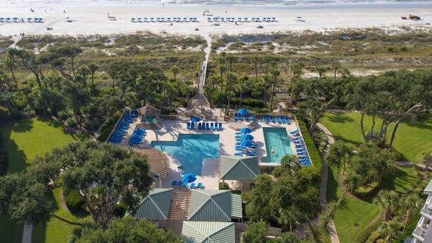 Un resort con una gran piscina, numerosas tumbonas y vistas a la playa.