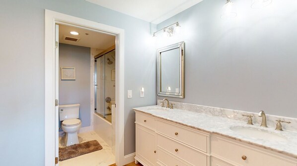 Une salle de bain avec des toilettes blanches, un grand meuble-lavabo doté d’un plan en marbre et un miroir au-dessus du lavabo.