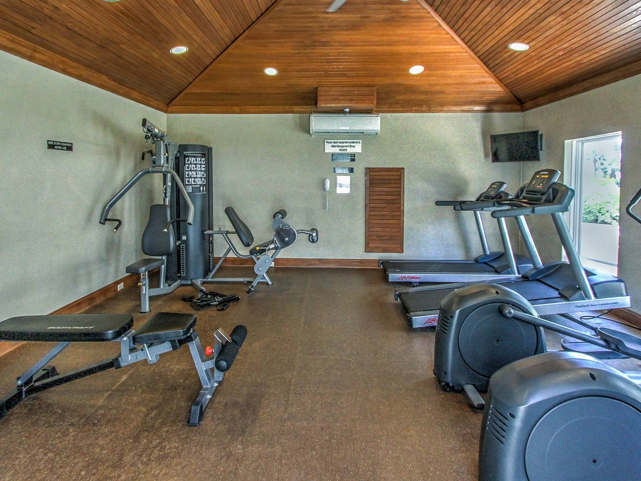 Un gimnasio con diversos equipos de ejercicio, incluyendo cintas de correr, una máquina de pesas y una banca.
