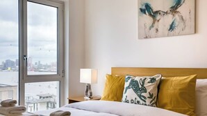 Et hotelværelse med en seng, et natbord, en lampe og et vindue med udsigt over byen.