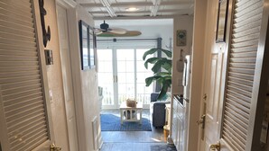 Een hal met houten vloer, witte deuren met verstelbare lamellen en een plafondventilator.
