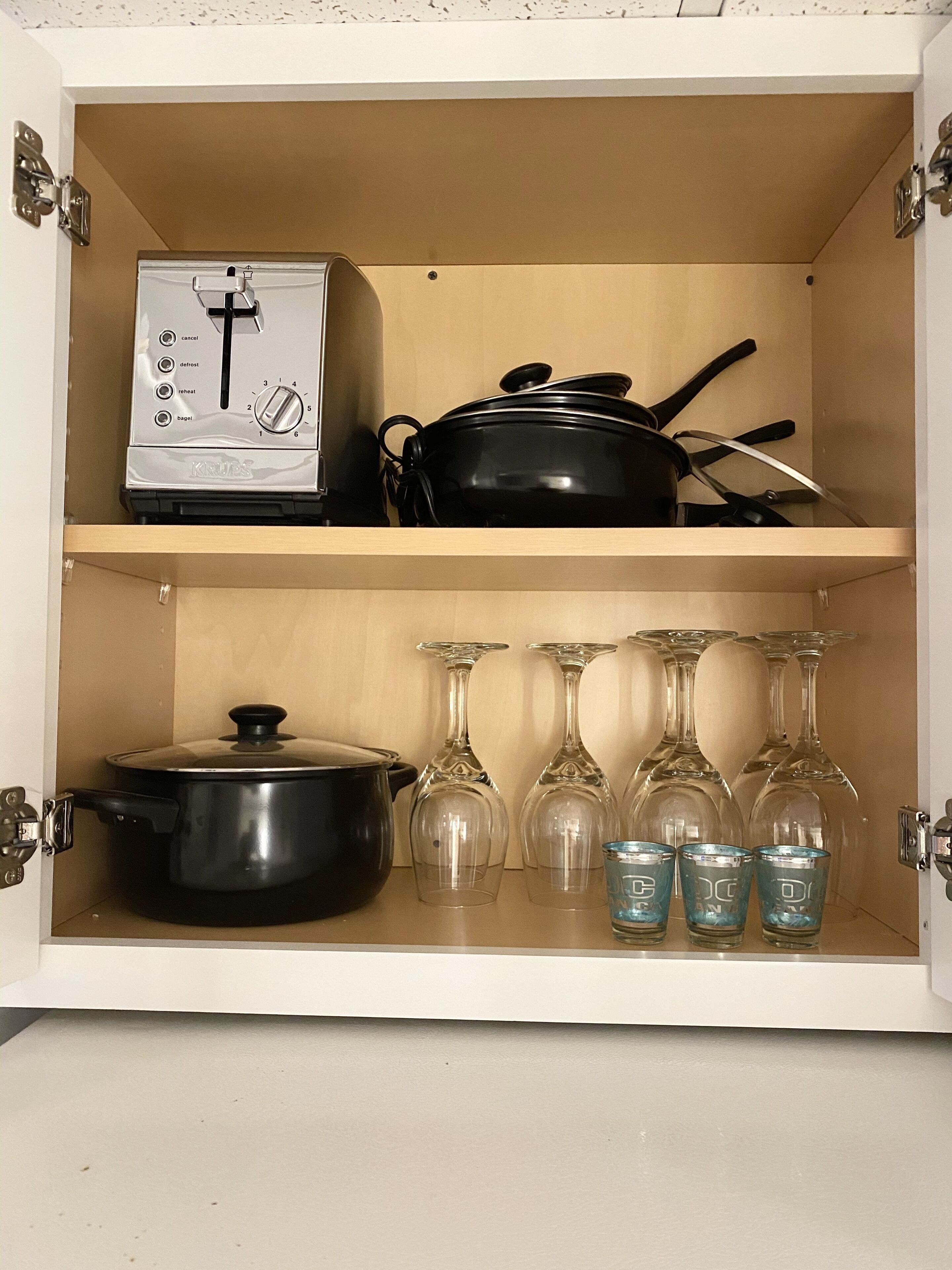 A kitchen cabinet with a kettle, a pot, and wine glasses.