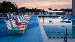 Een zwembadgedeelte met ligbedden en parasols, een zwembad met een metalen trap, en een uitzicht op de zonsondergang over het water.