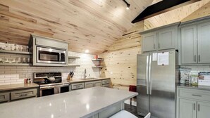 A modern kitchen with a wooden ceiling, stainless steel appliances, grey cabinets, and a large island with bar stools. - Chic SoCo Studio | Balcony + Walkable Austin (Austin)