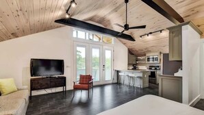 A spacious living area with a flat-screen TV, a sofa, and a red chair. A kitchen with a bar area is visible through the glass doors. - Chic SoCo Studio | Balcony + Walkable Austin (Austin)