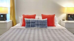 Un lit bien fait, avec une literie à motifs, deux oreillers rouges et un oreiller bleu et blanc.