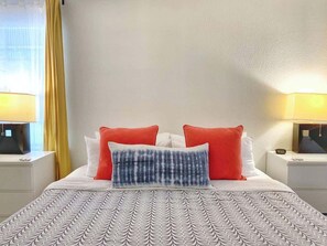 Un lit bien fait, avec une literie à motifs, deux oreillers rouges et un oreiller bleu et blanc.