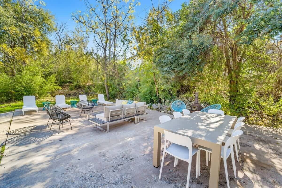An outdoor patio with a round table and chairs, surrounded by greenery and trees.