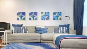 Ein modernes Wohnzimmer mit einer Eckcouch, einem blauen Teppich mit Muster und drei abstrakten Wandbildern.