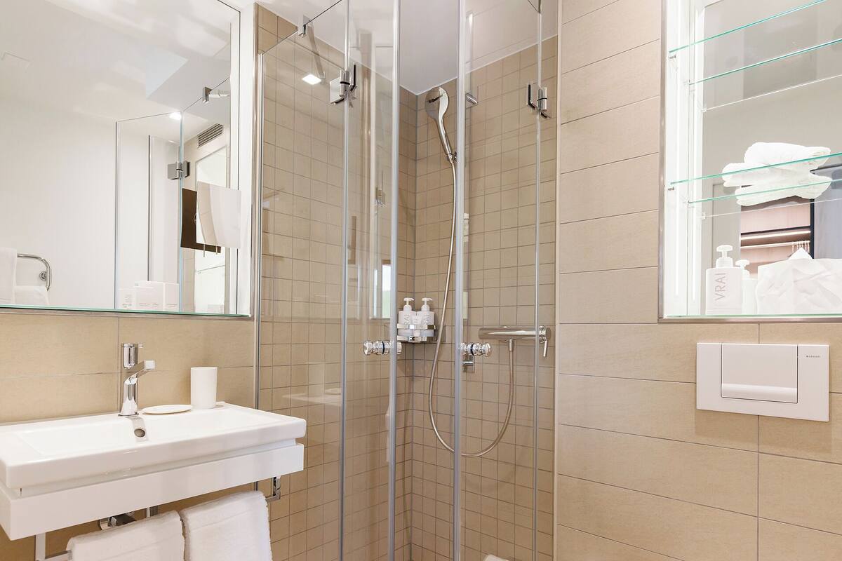 Ein modernes Badezimmer mit einer Duschkabine, einem weißen Waschbecken mit Spiegel darüber und einer Glasablage für Pflegeprodukte.