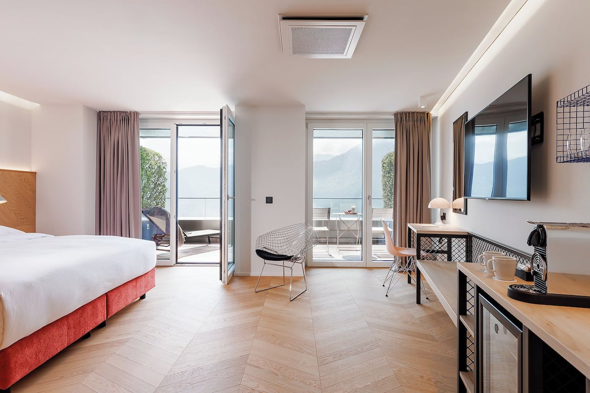 Ein Hotelzimmer mit Bett, Schreibtisch, Stuhl und einem Balkon mit Bergblick.