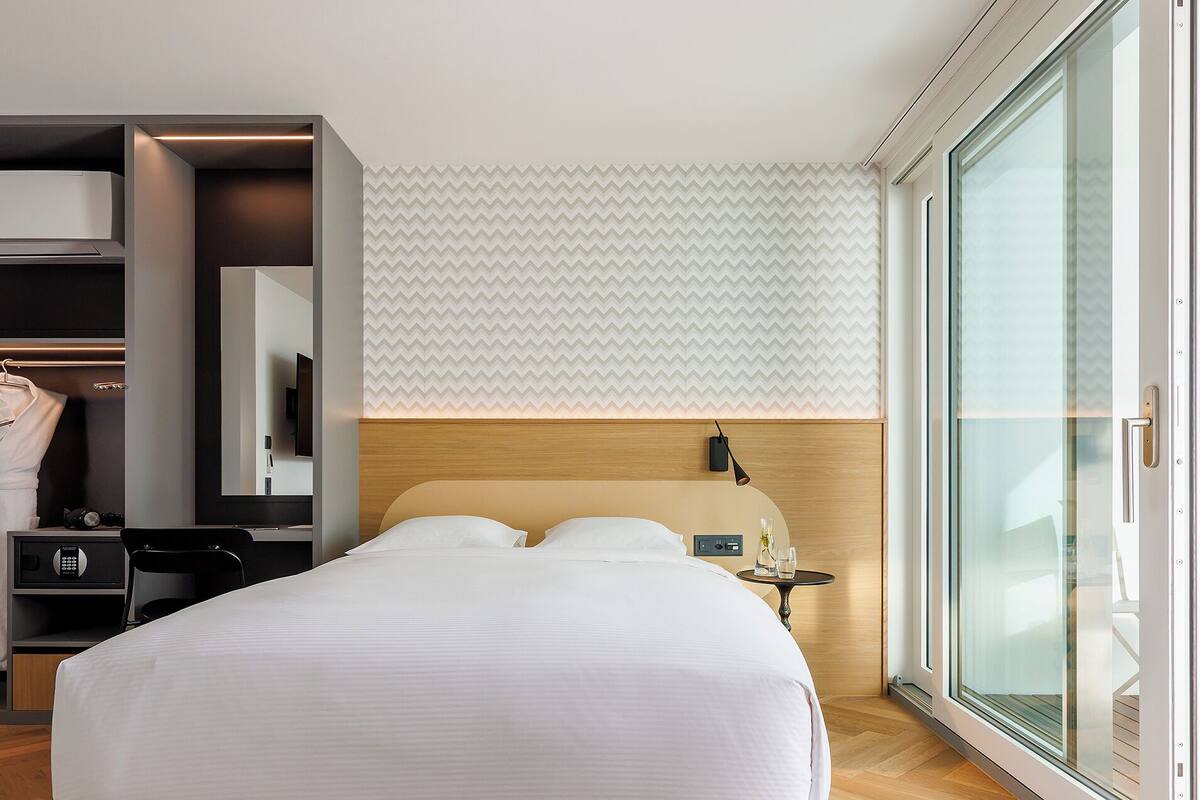 Ein modernes Hotelzimmer mit einem großen Bett, einem Kleiderschrank, einem Schminktisch und einem großen Fenster mit Blick.