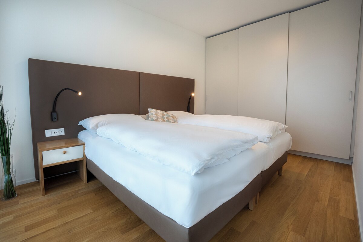 A neatly made bed with white linens, a bedside table with a lamp, and a wardrobe in a modern room.