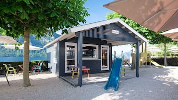Un petit espace de jeux extérieur avec un toboggan, des chaises colorées et un coin salon abrité.