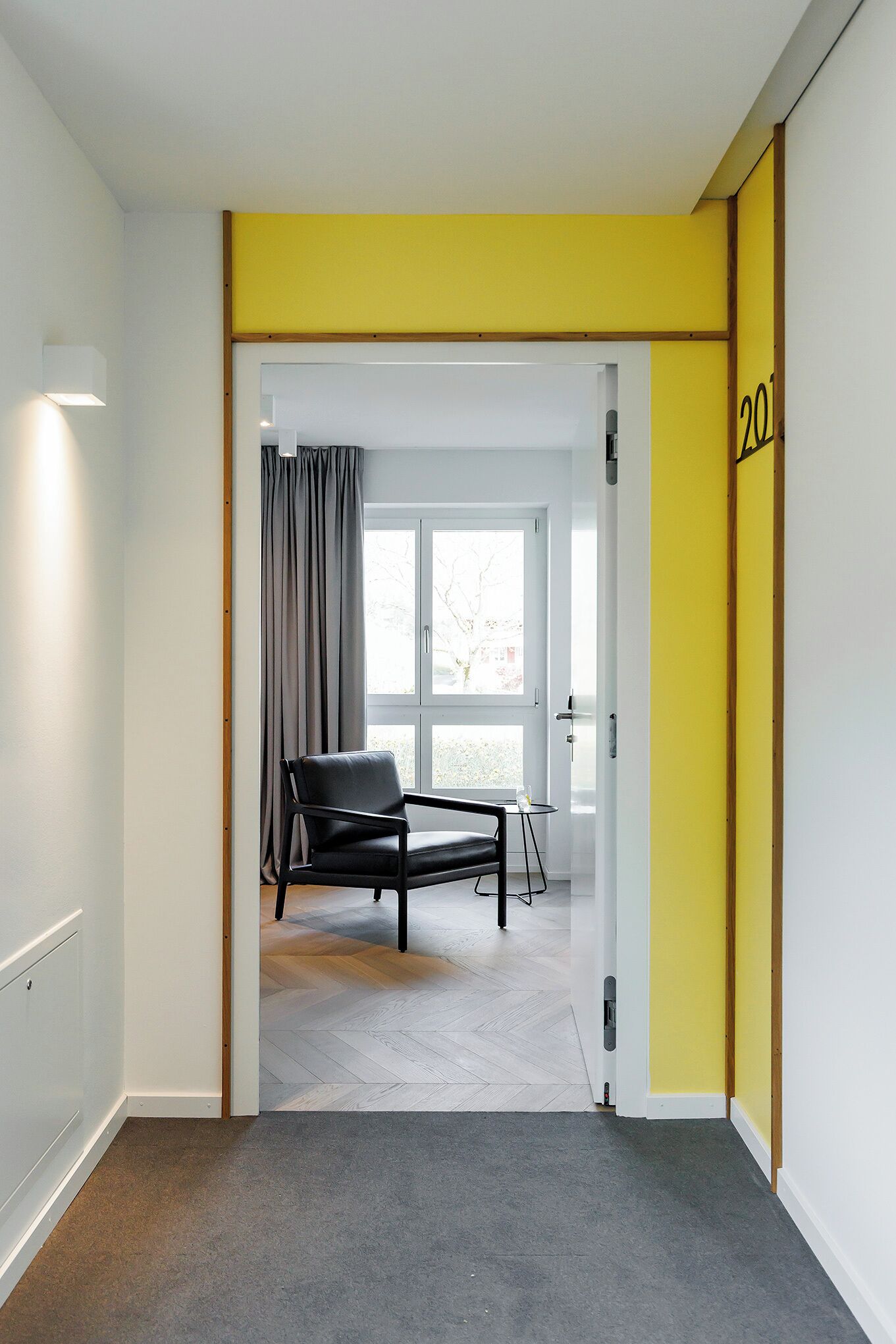A room with a grey carpet, a black chair, and a small table. A yellow door frame is visible on the right side.