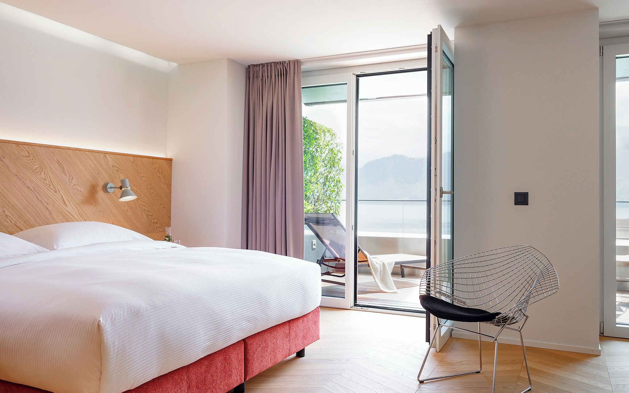 A hotel room with a bed, a chair, and a view of the outdoors.