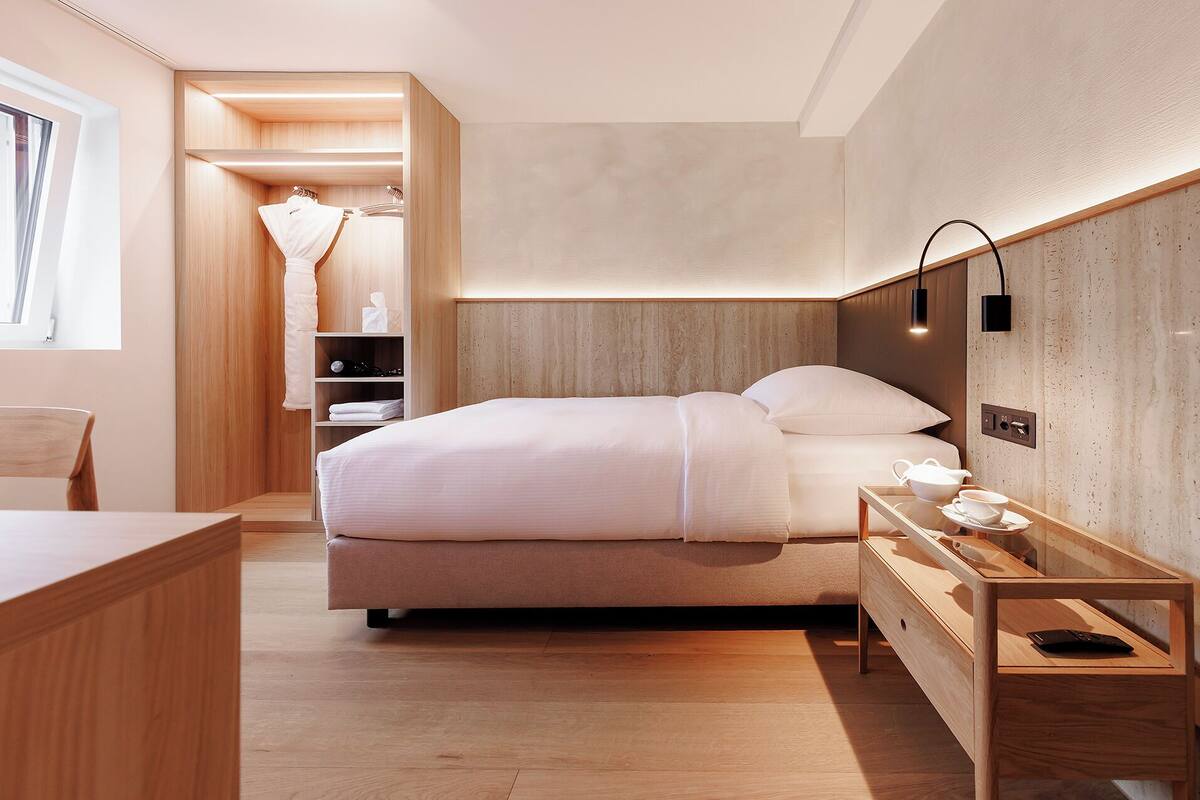 Ein modernes Hotelzimmer mit einem großen Bett, einem Nachttisch und einem kleinen Schreibtisch mit Stuhl.