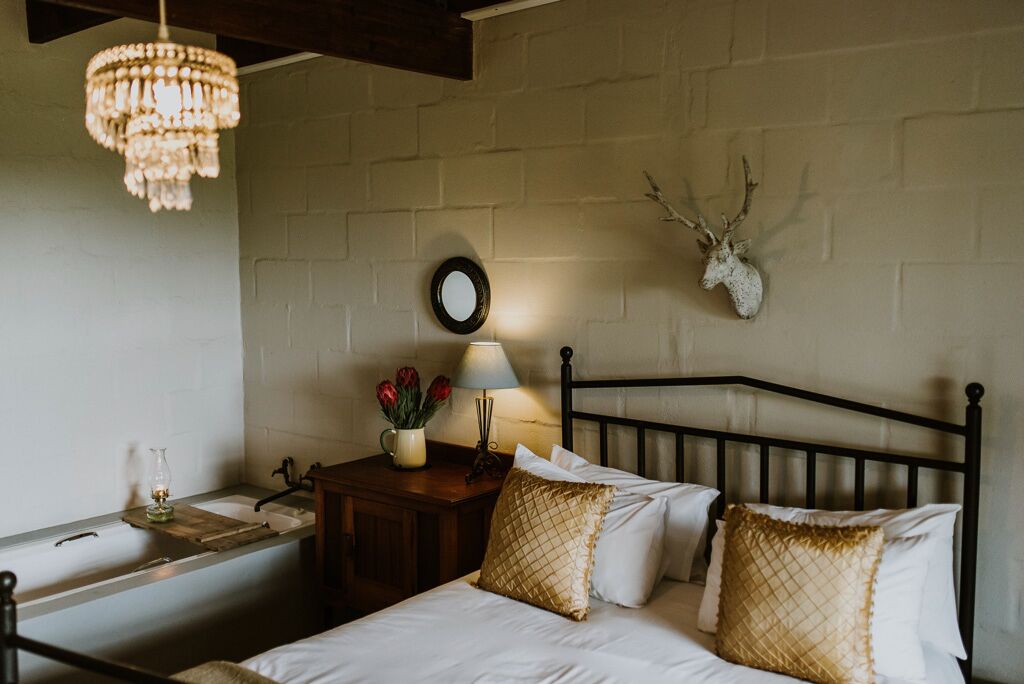 Un dormitorio con cama, mesita de noche, lámpara y una decoración de cabeza de venado en la pared.