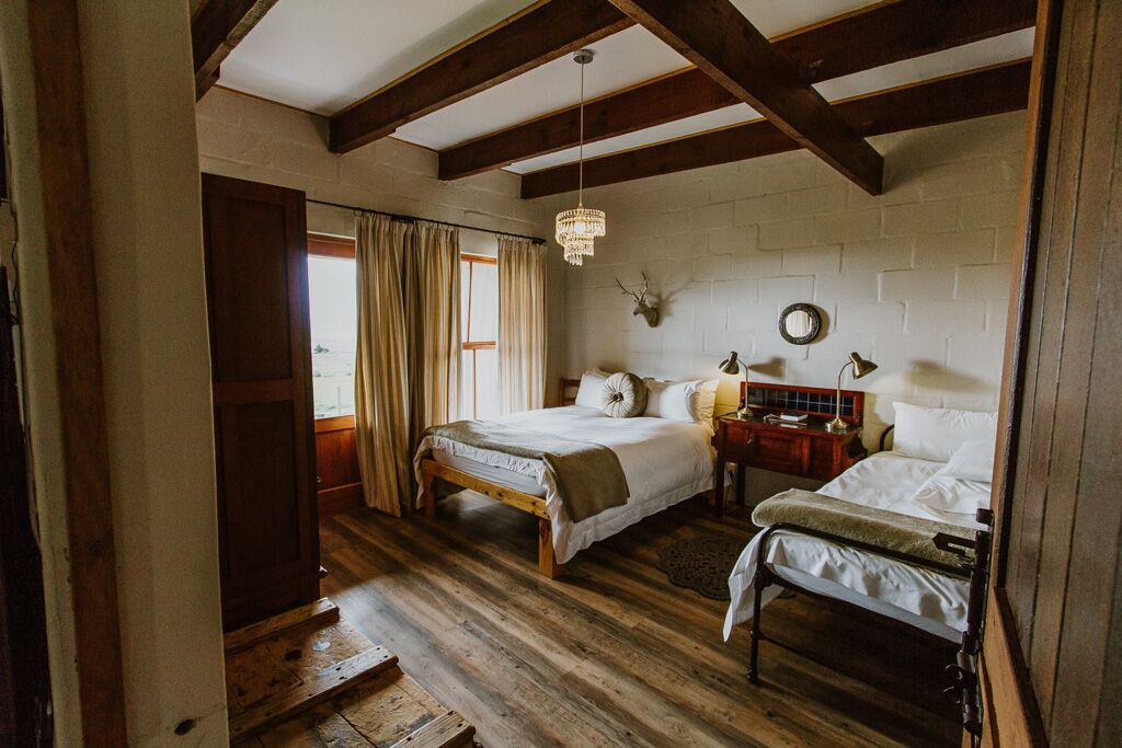 A bedroom with two beds, wooden flooring, a chandelier, and a brick wall.