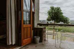 Puerta de madera que da a un balcón con una silla de metal y un cubo.