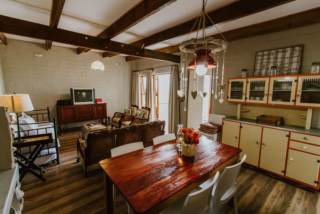 A rustic kitchen with wooden beams, a dining table with chairs, a wooden bench, and a hanging light fixture.