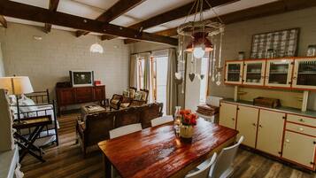 A rustic kitchen with wooden beams, a dining table with chairs, a wooden bench, and a hanging light fixture.