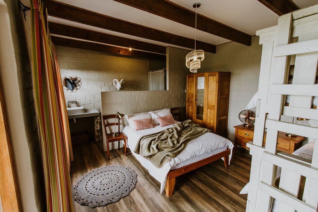 A bedroom with a wooden bed, a bedside table, a hanging chandelier, and a white brick wall.