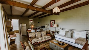 A cozy living room with a sofa, chairs, a coffee table, and a kitchen in the background. - The Stables Cottages (Langebaan)