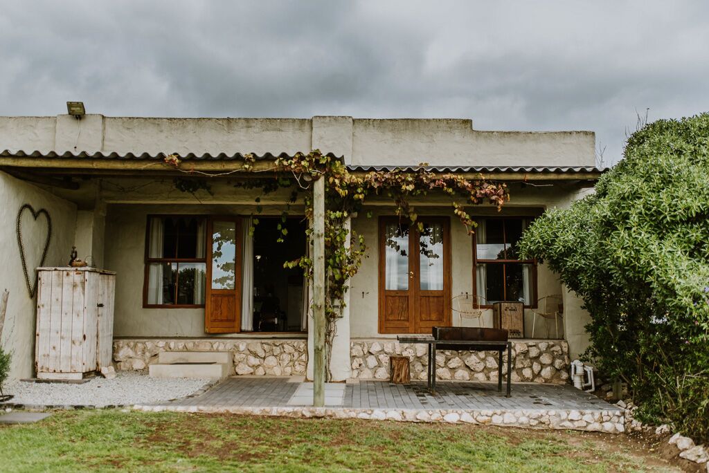 Une maison avec des fondations en pierre, des portes en bois et une véranda couverte avec une table et des chaises.