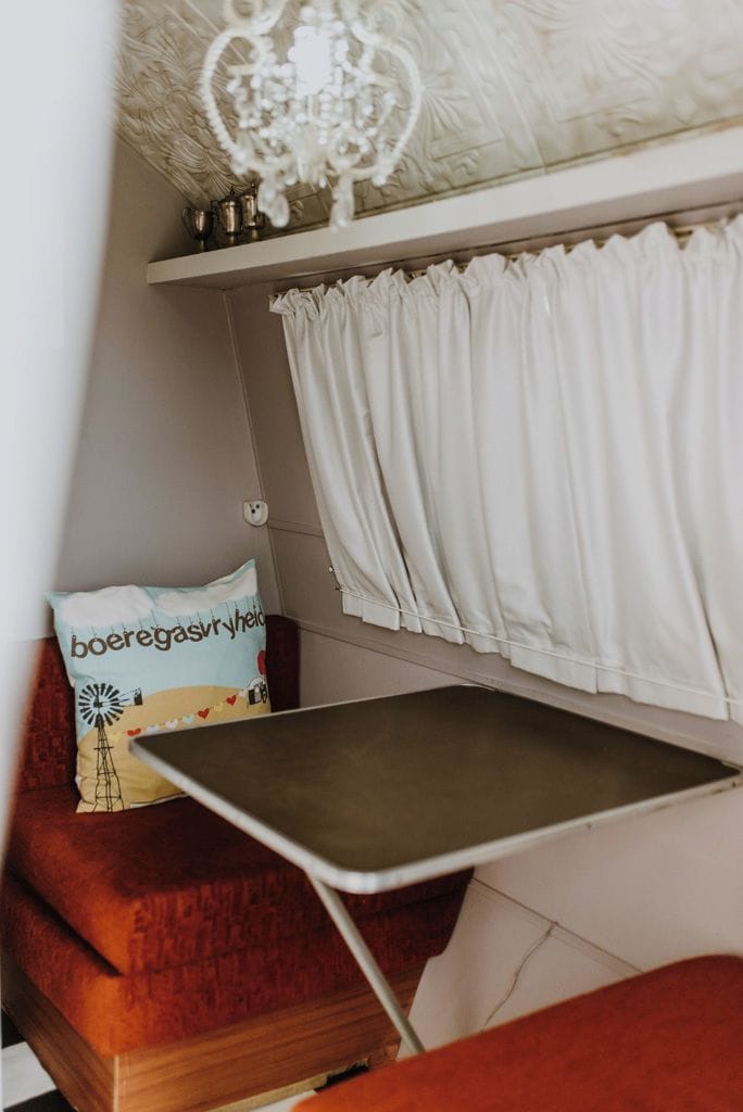 Ein Zimmer mit einem Bett, einem kleinen Tisch, einem Zierkissen, einer Kronleuchter und Vorhängen.