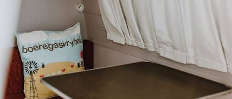 Ein Zimmer mit einem Bett, einem kleinen Tisch, einem Zierkissen, einer Kronleuchter und Vorhängen.