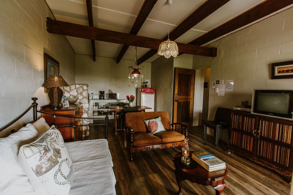A cozy living room with a sofa, a wooden coffee table, and a television. There is a kitchen area in the background with a refrigerator and a sink.