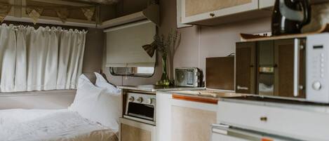 A compact bedroom with a bed, a small kitchenette with a stove, a microwave, and a toaster.