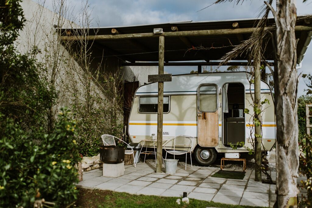 A white RV parked under a wooden structure with a covered patio area, surrounded by greenery.