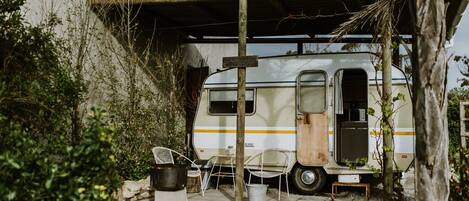 A white RV parked under a wooden structure with a covered patio area, surrounded by greenery.