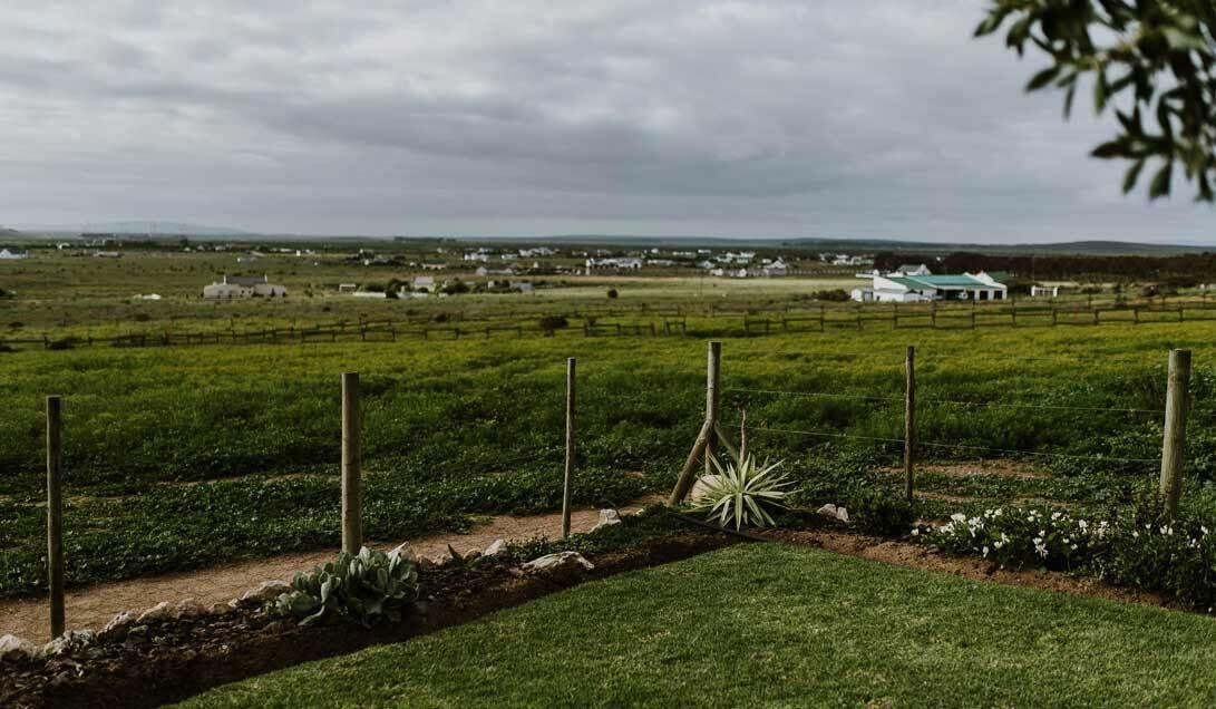 A rural landscape with fields, a fenced area, and a distant white building.