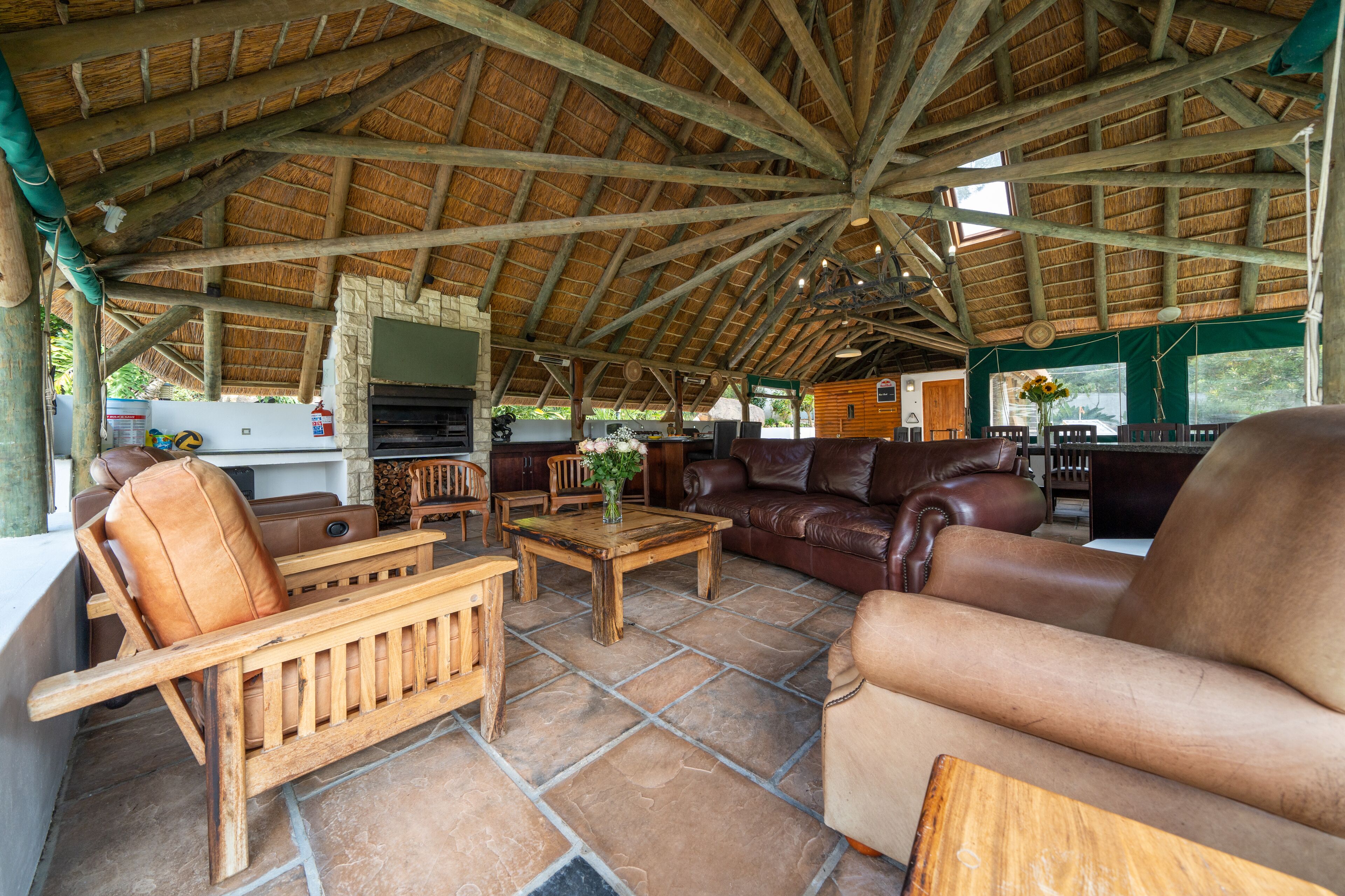 An outdoor covered patio with wooden furniture, a stone floor, and a thatched roof.