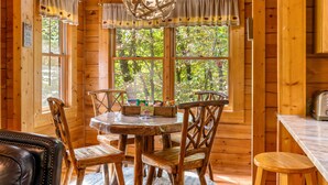 Interior de una cabaña de madera con una mesa de comedor, sillas y una zona de cocina.