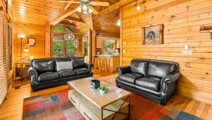Interior acogedor de una cabaña con dos sofás de cuero, una mesa de comedor de madera y una zona de cocina.