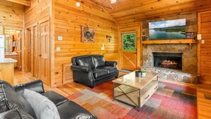 Interior acogedor de una cabaña con chimenea, paredes de madera, un sofá de cuero negro y un televisor sobre la chimenea.