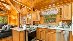 Interior de una cabaña de madera con cocina equipada: estufa, horno, fregadero y lavavajillas.