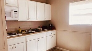 Une petite cuisine avec des meubles blancs, un four à micro-ondes, une cuisinière et une machine à café.