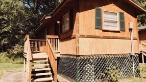 Une cabane en bois avec un escalier menant à une terrasse, entourée d’une clôture en treillis et de verdure.