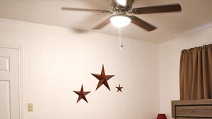Une chambre à coucher comprenant un lit, un ventilateur de plafond, une table de chevet, une lampe et des décorations murales en forme d’étoiles.