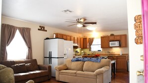 Un salon comprenant un canapé beige, un canapé marron et un coin repas avec des meubles de rangement en bois et un four à micro-ondes.