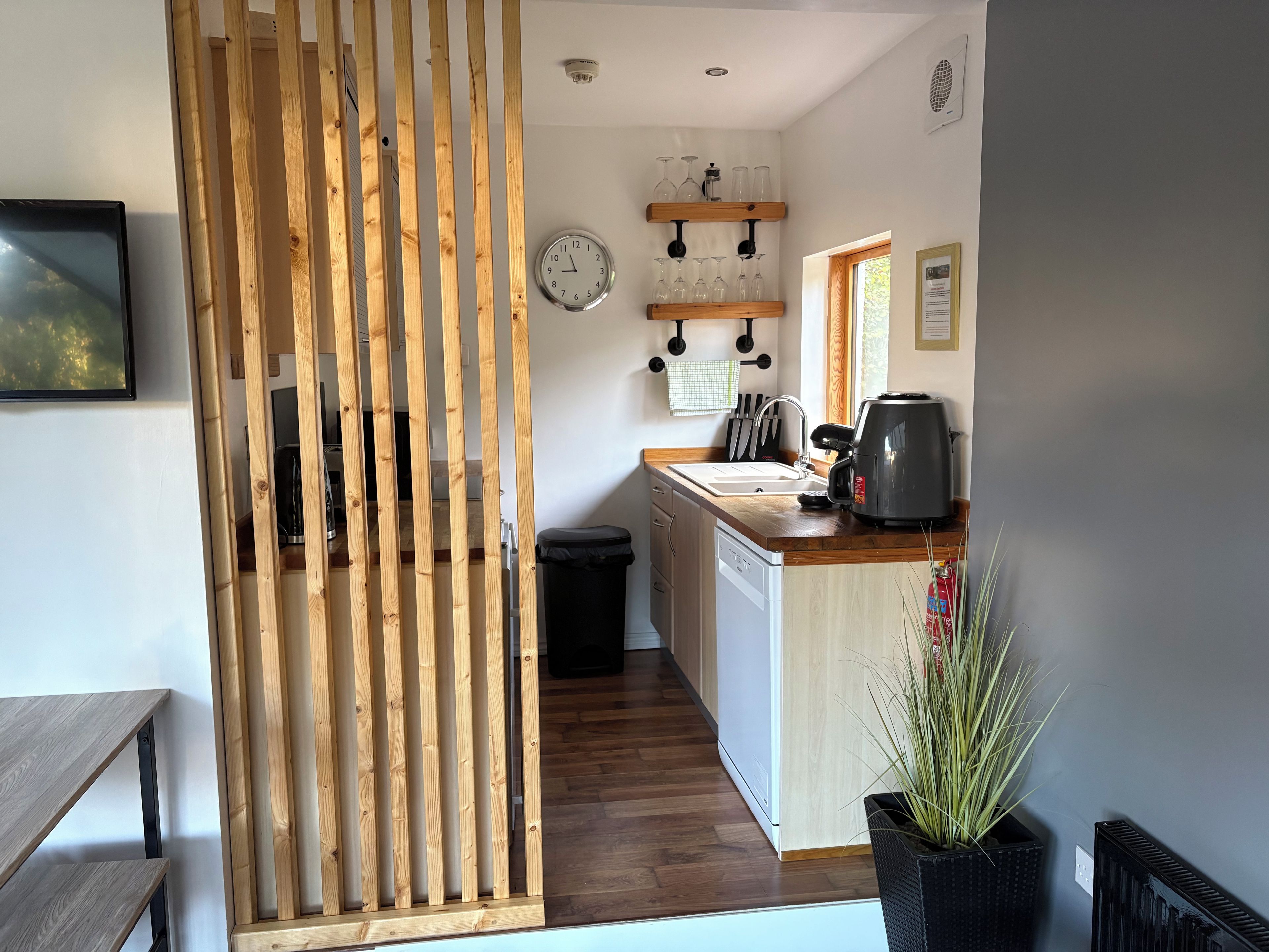 A modern kitchen with wooden slats, a clock, wine glasses, and a coffee maker.